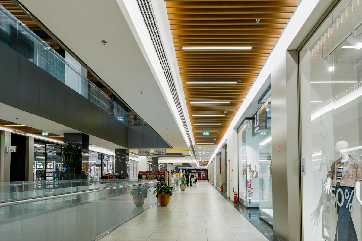 Prema zahtevima investitora, na koridorima ispred radnji izvedena je promena plafona, pri čemu su linijske svetiljke Slotlight Infinity Pendant elegantno uklopljene između "bafli", odnosno drvenih letvica. Dodatno svaka četvrta svetiljka iz ove serije opremljena je EM modulom / foto: Dragana Udovičić